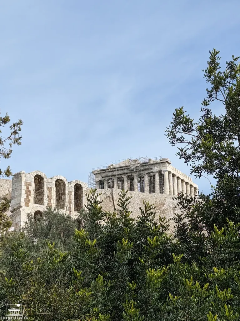 The Parthenon and the Odeon of Herodes Atticus on the Acropolis of Athens, partially obscured by trees.