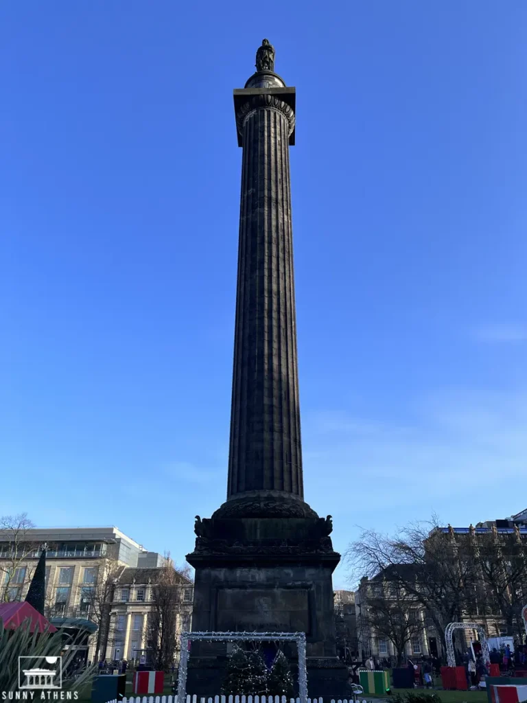 A towering column with a statue atop in St. Andrew Square Garden, set against a clear blue sky.