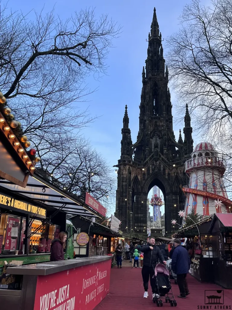 The towering Scott Monument, with holiday stalls at its base and people strolling around.