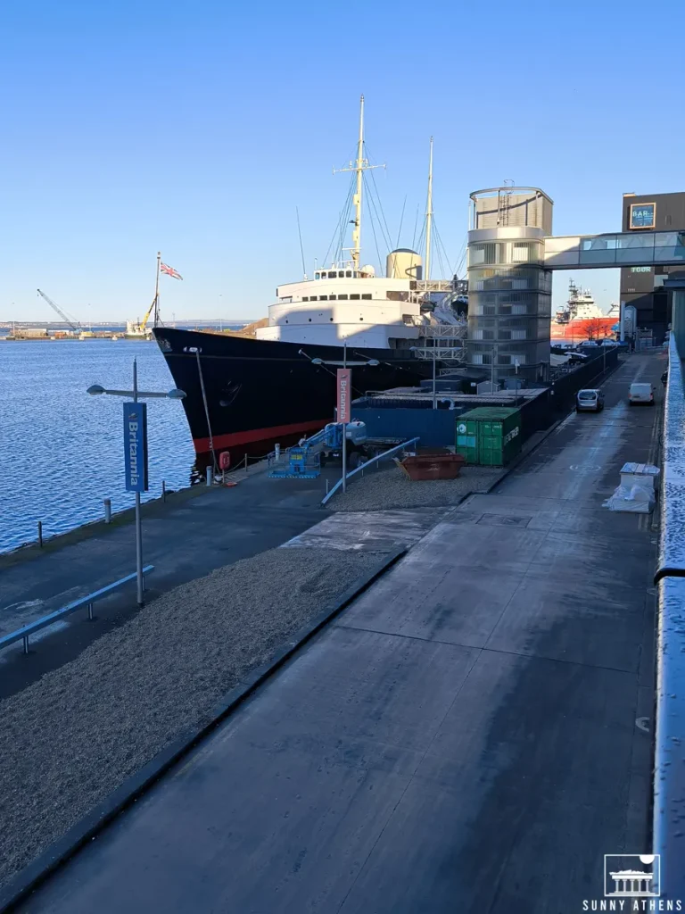 The Royal Yacht Britannia parked by the water with buildings nearby.