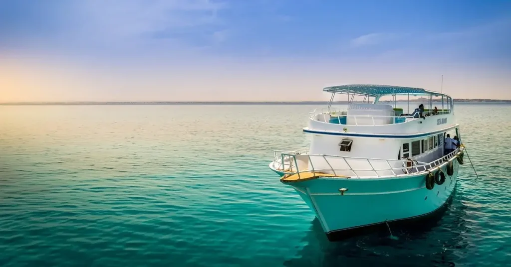 A tiny cruise boat sailing in calm turquoise waters under a sunset sky.