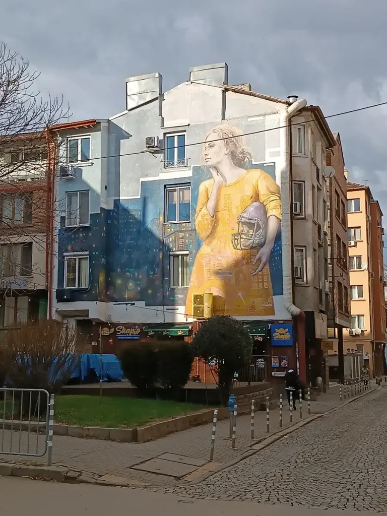 Graffiti of a woman in a yellow dress holding a baseball helmet, painted on a building wall.