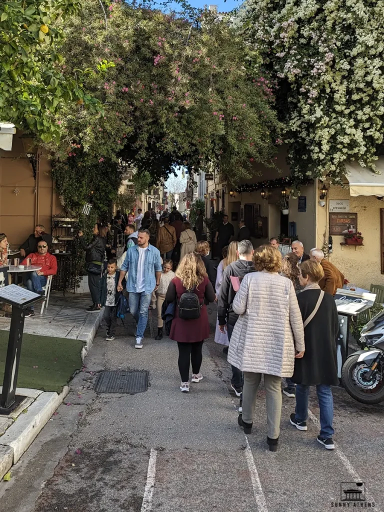 Best Season for Athens: crowded street in Plaka with people walking under flowers during the March 25th celebrations.