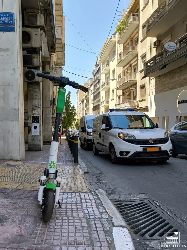 A Lime electric scooter parked on a sidewalk in the center of Athens.