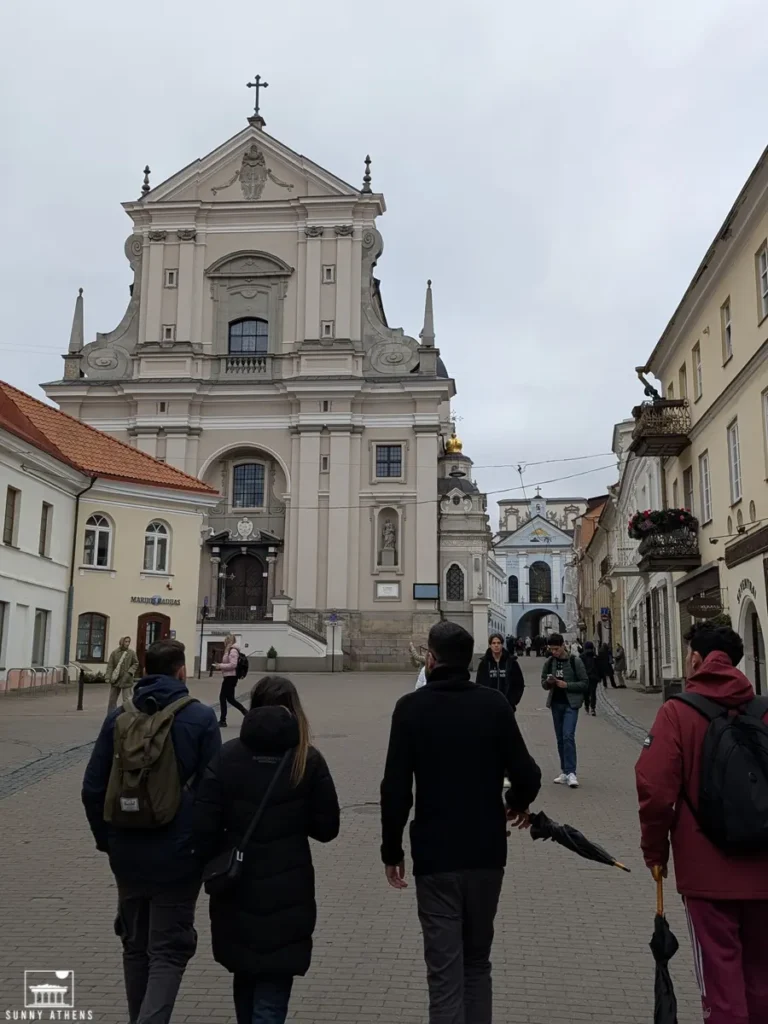 Four people walking on Didzioji Street with the facade of Church of St. Theresa on their left.