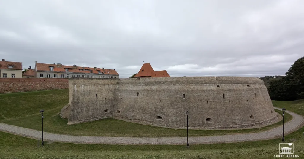 Side view of the Bastion of the Vilnius Defensive Wall, showcasing its rounded brick structure under a cloudy sky.