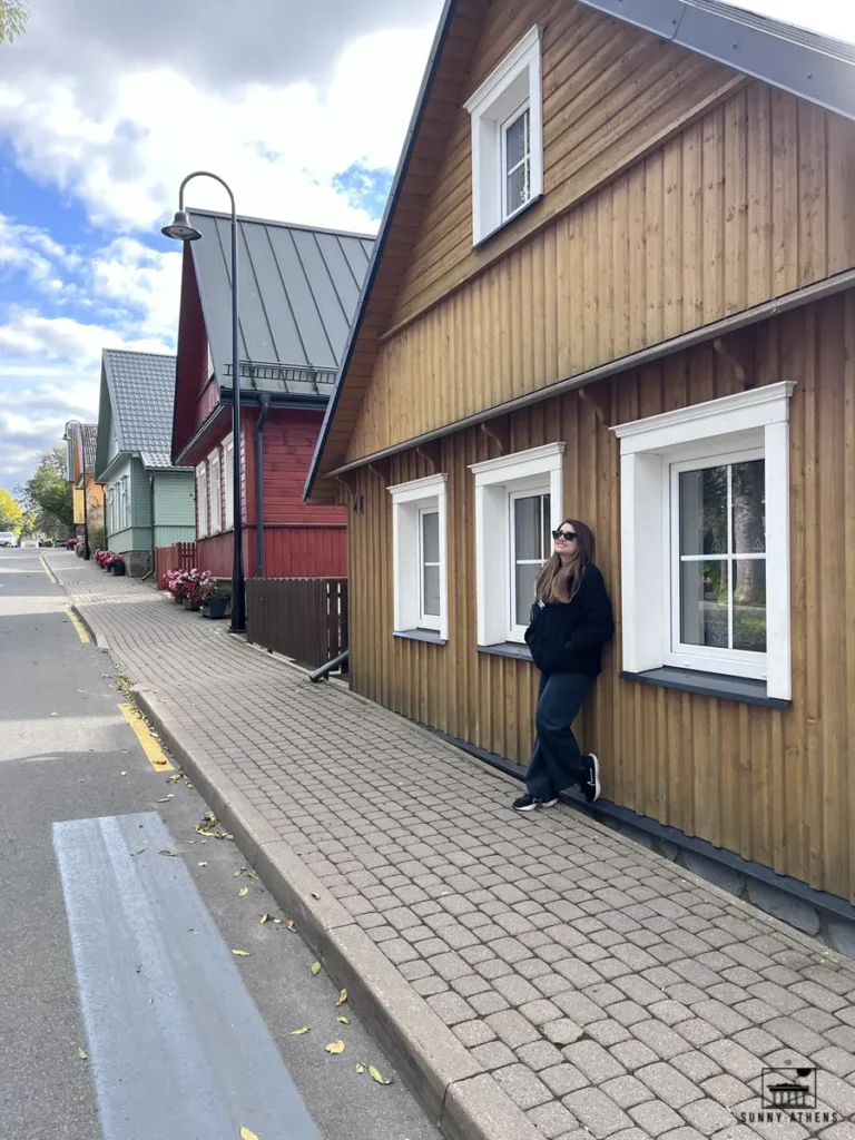 3 days itinerary of Vilnius: Chrysavgi leaning against a wooden house in Trakai, smiling and enjoying the peaceful surroundings.