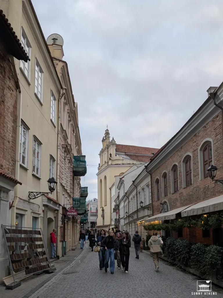 Pilies Street in Vilnius, lined with historic buildings, and people walking around.