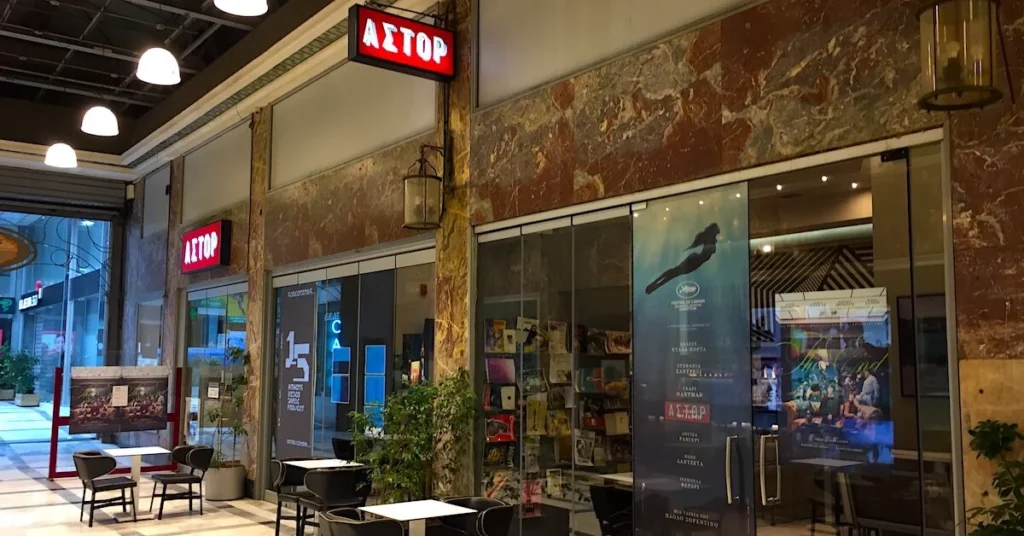 Best indoor cinemas in Athens center: The entrance of Astor cinema inside the arcade of Korai square with tables outside where the moviegoers can enjoy their coffee and drinks