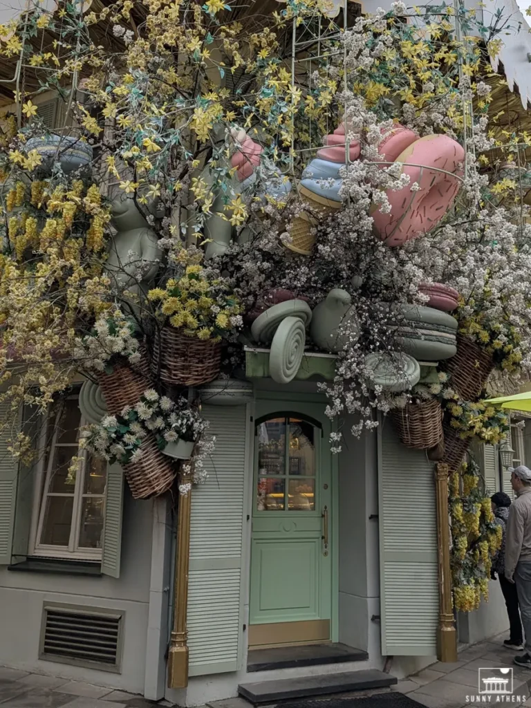 A small café entrance decorated with colorful flowers and huge plastic toys.