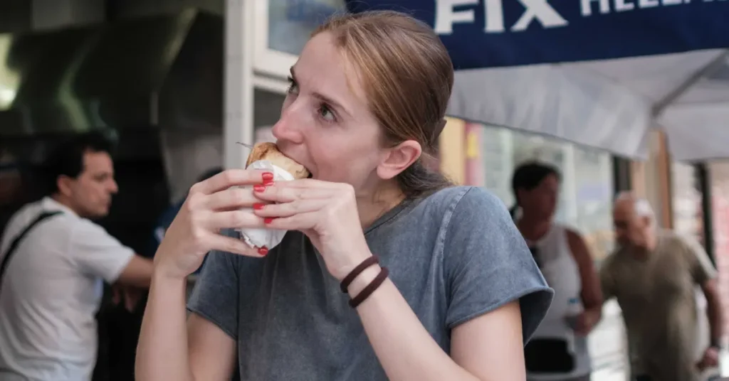 Best traditional souvlaki in Athens: A woman enjoys eating a pita wrap at an outdoor food stall.