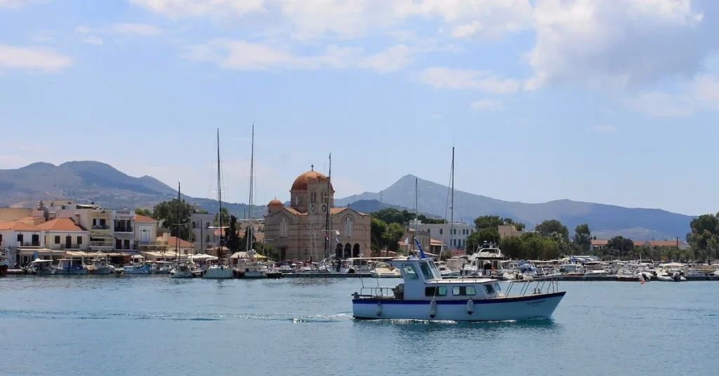 How to escape the crowds in Athens: View of the Port of Aegina island under the sun with a church in the background and a fishing boat in the foreground.