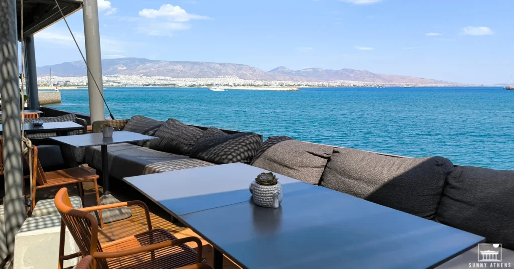 How to escape the crowds in Athens: Outdoor waterfront seating at Mikrolimano, Piraeus. with a view of the sea and Attica mountains in the background.