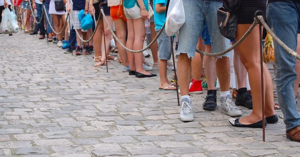 How to escape the crowds in Athens: People seen from the waist down waiting in queue on a cobblestone street.