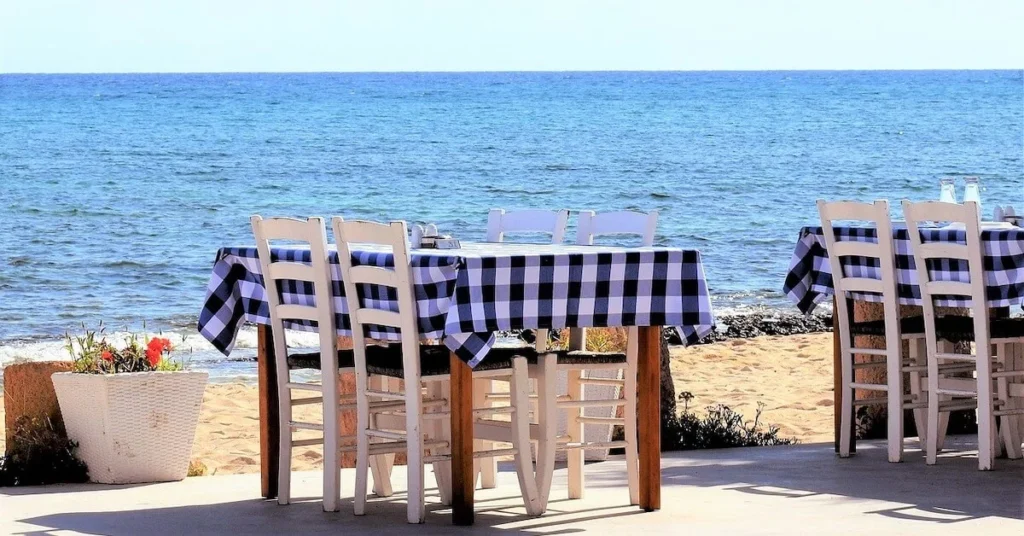 How to escape the crowds in Athens: Two tables with blue and white plaid tablecloth in a traditional seaside taverna under the sun.