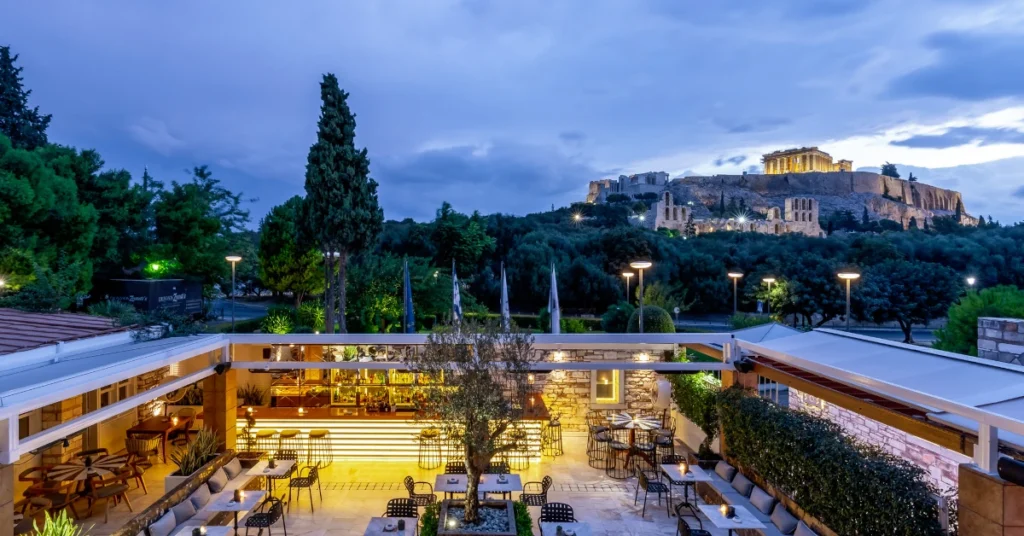 The stylish open-air restaurant of Dionysos Zonar's with a stunning view of the illuminated Acropolis at dusk.