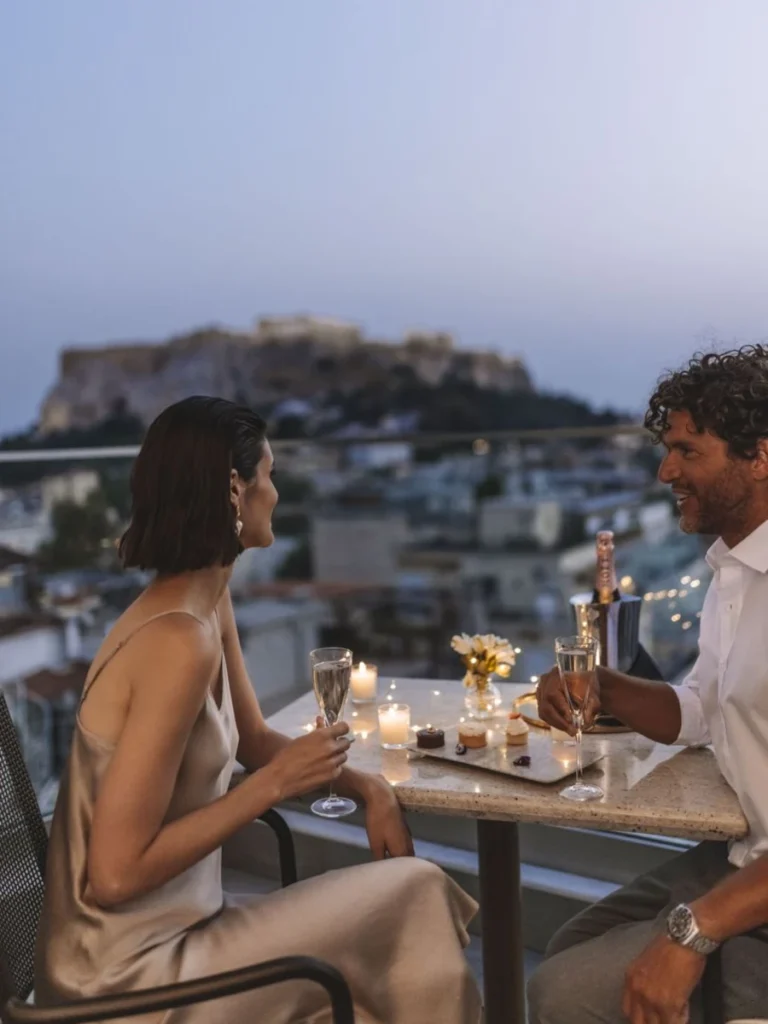 Honeymoon in Athens: A couple enjoying a candlelit dinner with a breathtaking view of the illuminated Acropolis at Electra Metropolis Athens.