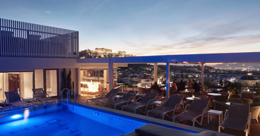 Honeymoon in Athens: The rooftop pool and lounge area of Electra Metropolis with a panoramic view of Athens and the Acropolis at sunset.