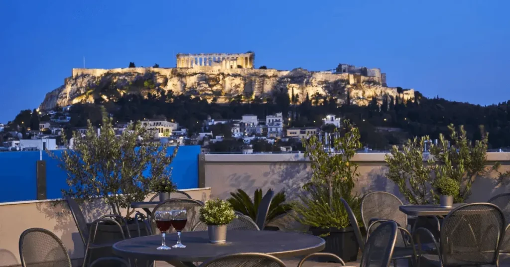Evening view of the Acropolis from the roof restaurant of Arion Hotel in Psiri, Athens, with a couple of glasses with wine on the foreground and the illuminated Acropolis hill on the background.