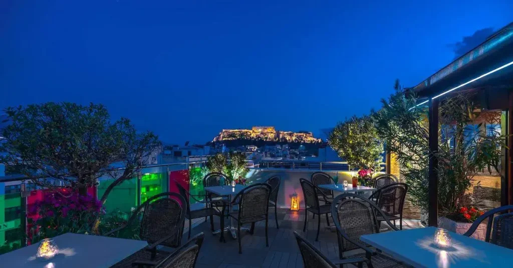 Night view from the roof restaurant of Attalos Hotel in Psiri, Athens, with a few candle lit tables in the foreground and the illuminated Acropolis Hill on the background.