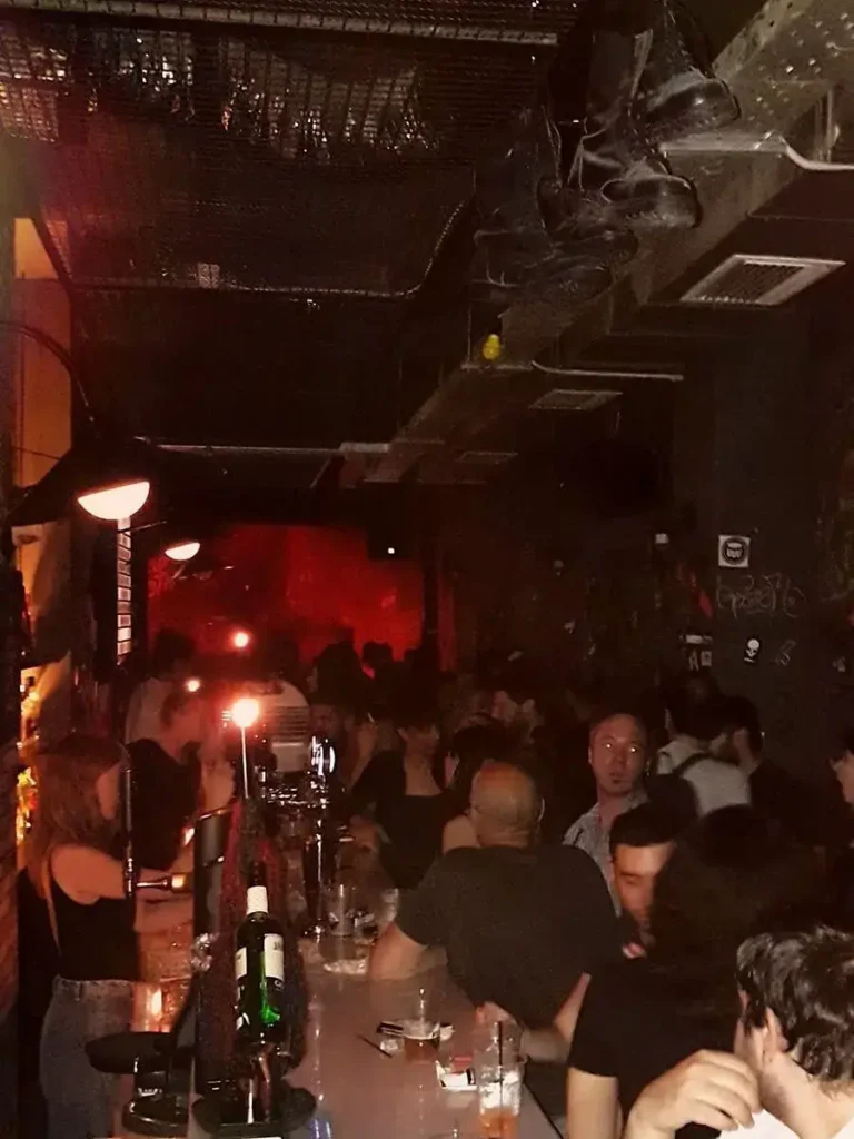 Internal view of Bad Tooth bar, with patrons standing or sitting at the bar and a live gig happening in the background.