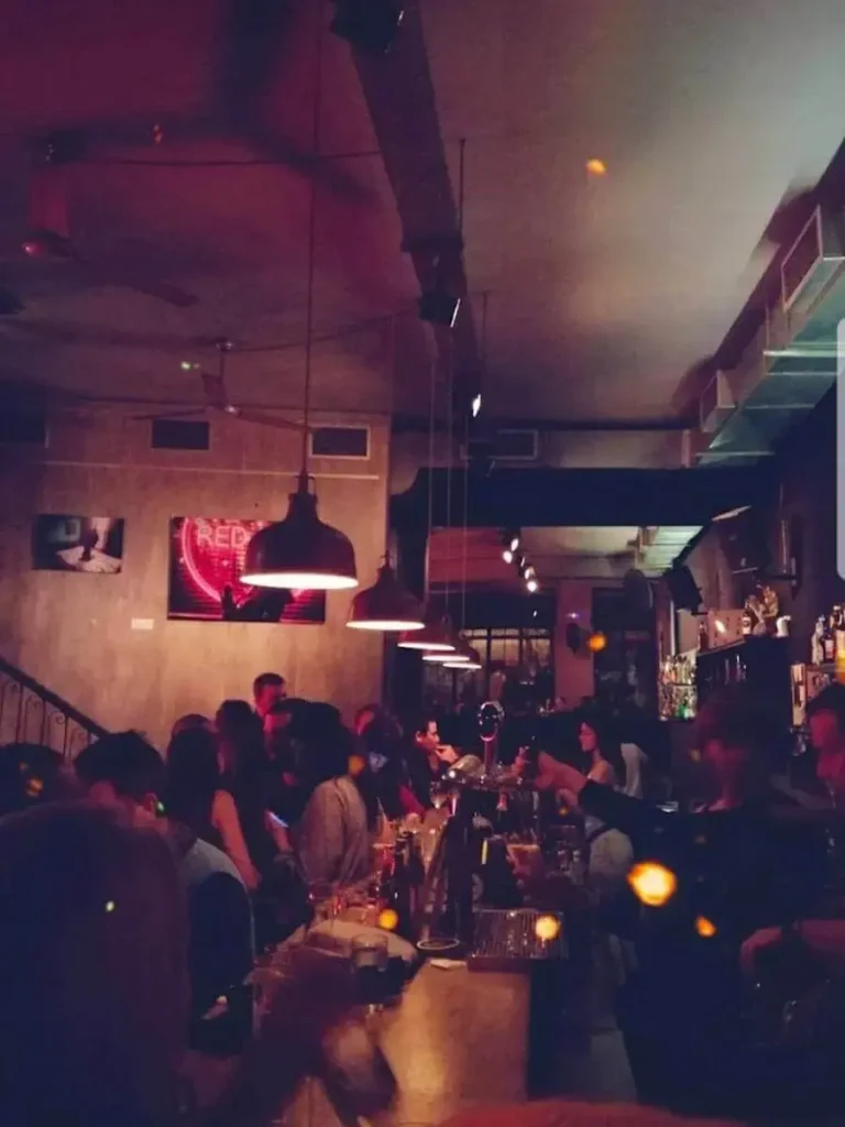 View of the bar in red and green hues in Barrett bar, with patrons at the bar talking and drinking.