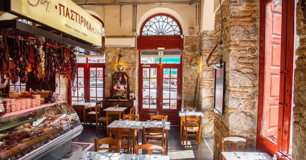Interior sunlit view of the Karamanlidika tou Fani deli-restaurant in Psiri, Athens, with a few tables set up.