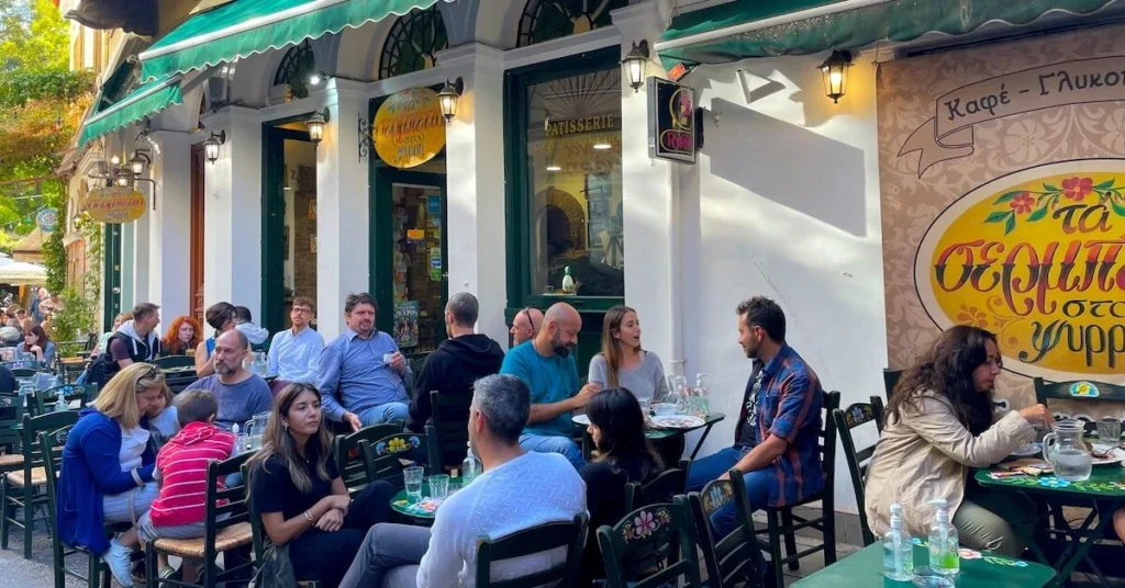 External afternoon view of the traditional patisserie Ta Serbetia stou Psiri with patrons sitting on the tables and enjoying their sweets.