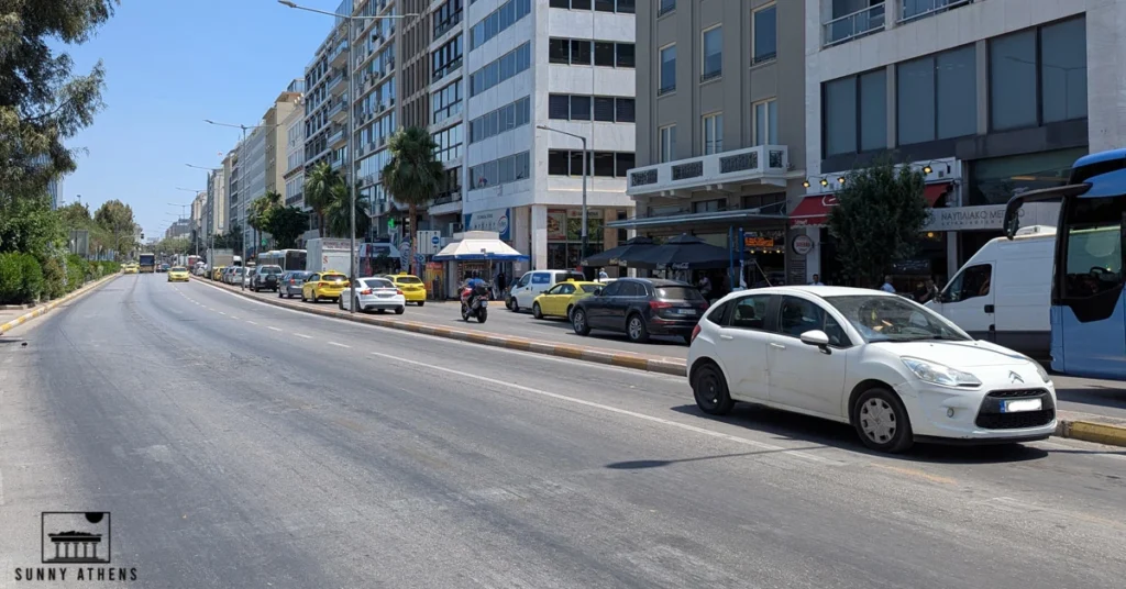 Street view of Akti Miaouli Avenue in Piraeus with a white car in the center, and modern buildings in the background.