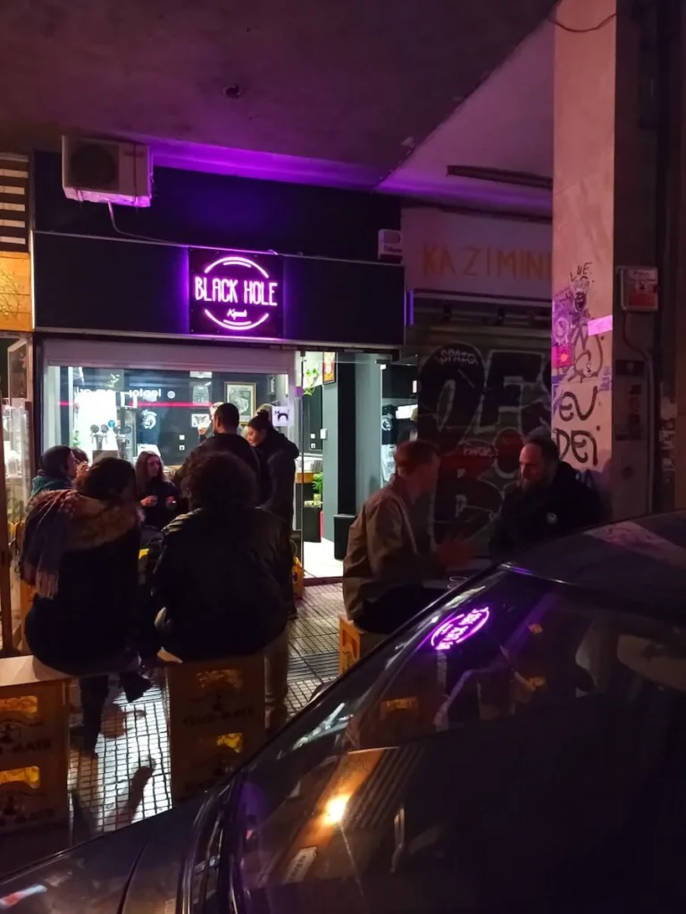 Night view from the steet of Black Hole tap-room in Kypseli with people sitting outside enjoying their beer