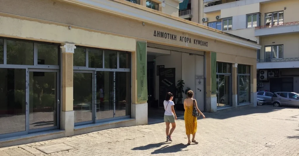 Kypseli Athens Travel Guide: Two women walk in front of the Municipal Market of Kypseli in Fokionos Negri drenched in afternoon sunlight