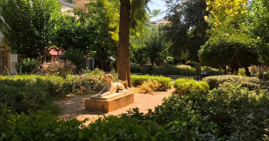 View of one of the gardens in Fokionos Negri pedestrian street in Kypseli with a lot of greenery and the famous statue of a dog in the afternoon sun
