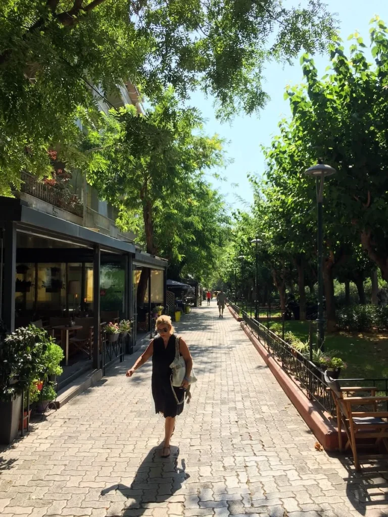 View of Fokionos Negri pedestrian street in Kypseli with a woman walking in front of a cafe in the afternoon sun