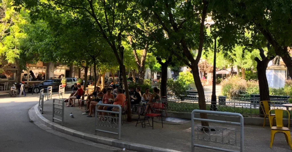 Kypseli Athens Travel Guide: View of Agios Georgios square in Kypseli with patrons sitting at tables on the square enjoying coffee and drinks in the shade under the trees