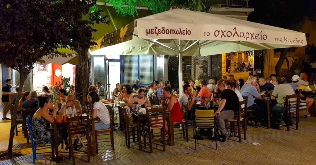 Night view of the tables of Scholarchio Tiw Kypselis restaurant on Agios Georgios square with patrons sitting at the tables enjoying their mezedes and drinks