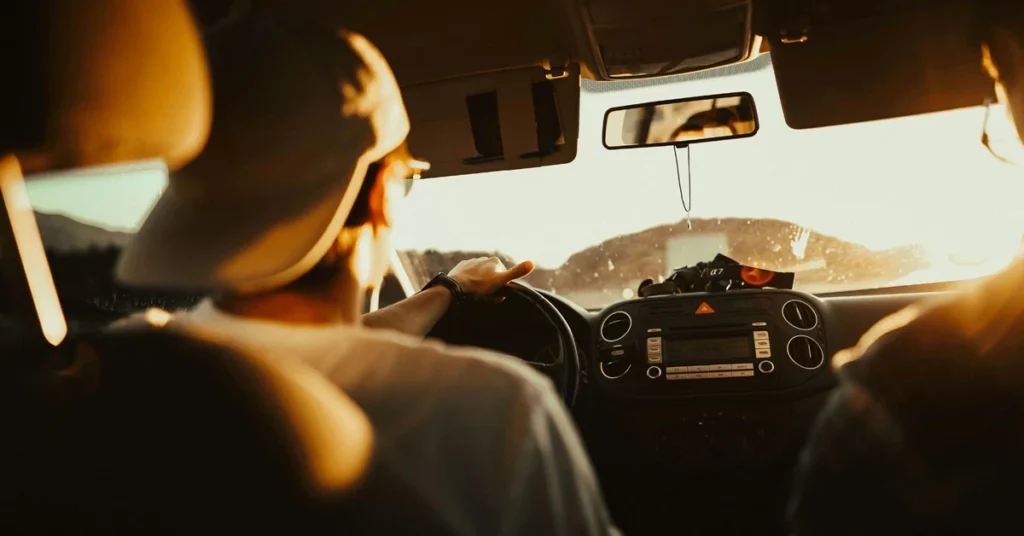 Two people driving a car at sunset.