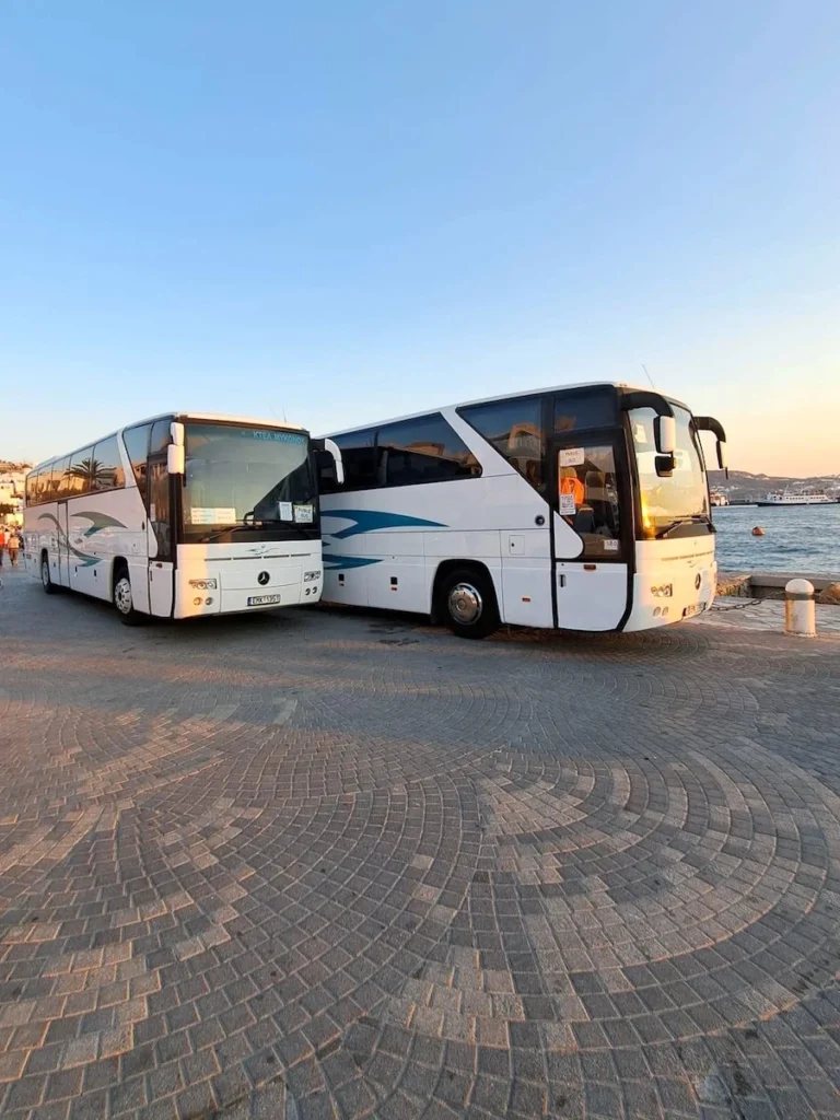 Two KTEL buses parked by the sea in Mykonos at sunset.