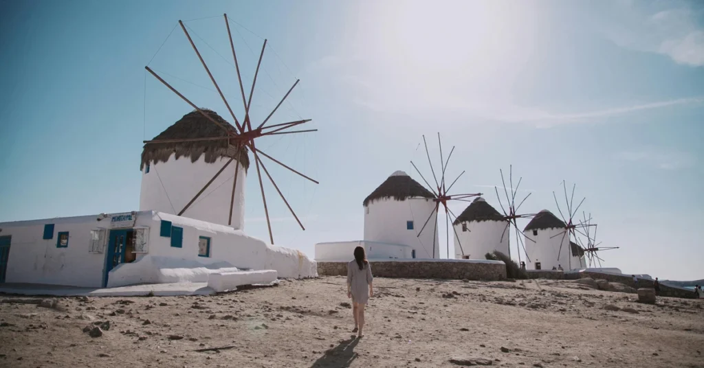 A woman walking towards the famous windmills of Mykonos on a sunny day.