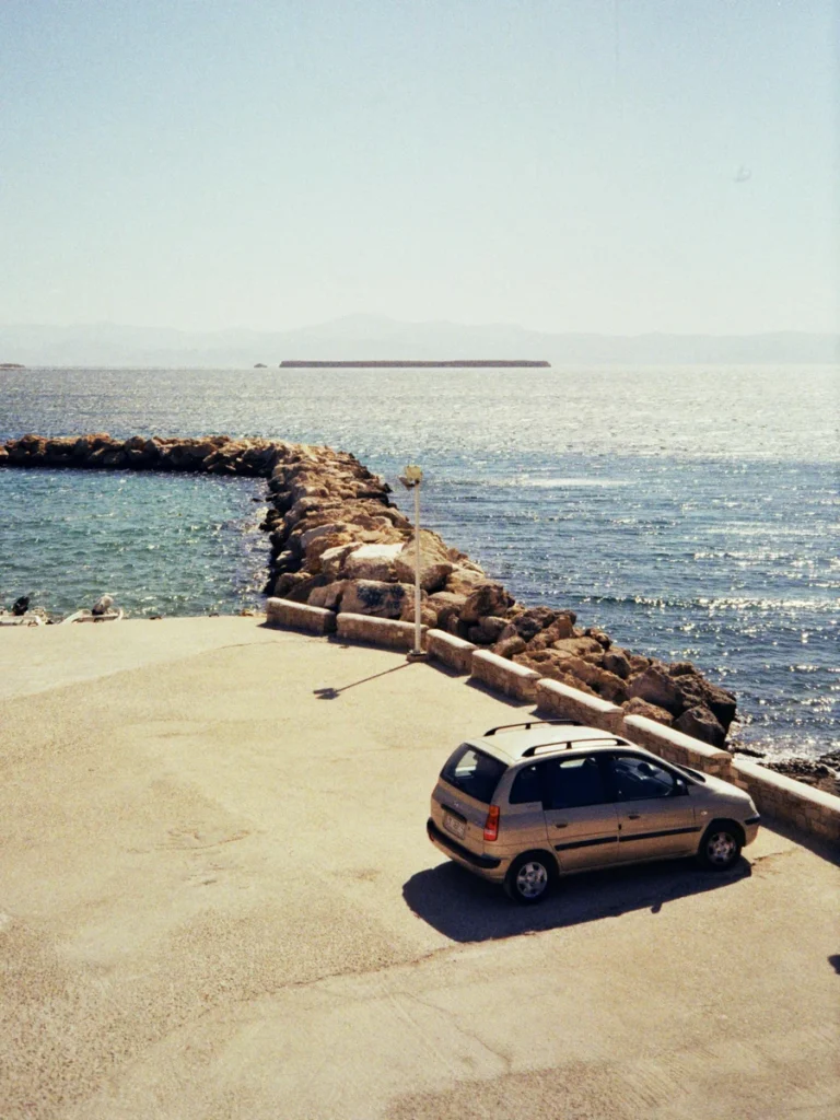 A small rental car parked next to a stone pier by the sea.