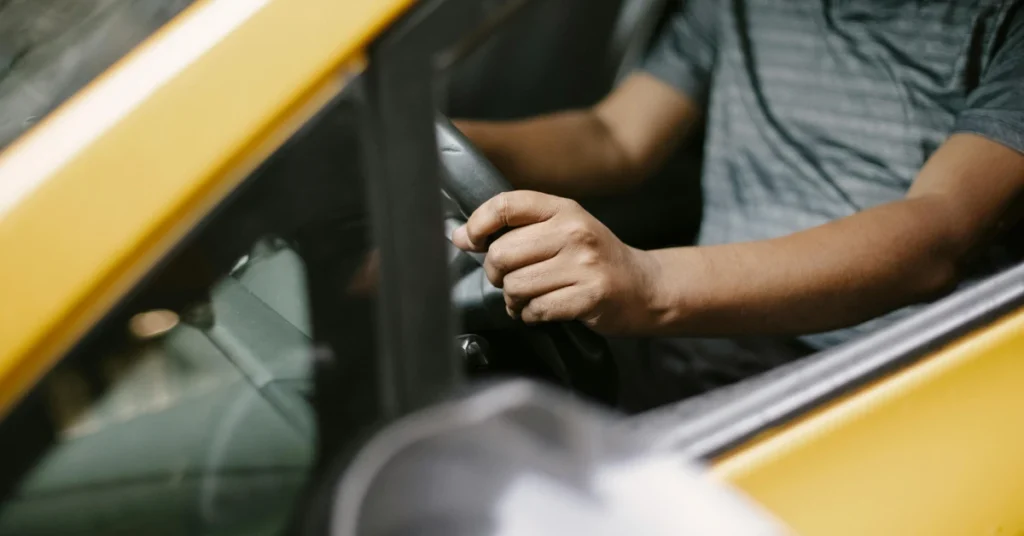 A taxi driver holding the steering wheel of a yellow cab.
