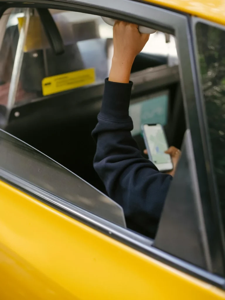 A passenger in the back of a yellow taxi holding a grab handle while using their smartphone.