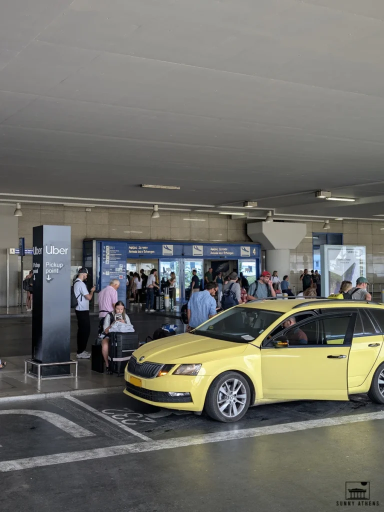A yellow taxi in front of the Uber pickup point at Gate 4 of Athens International Airport.