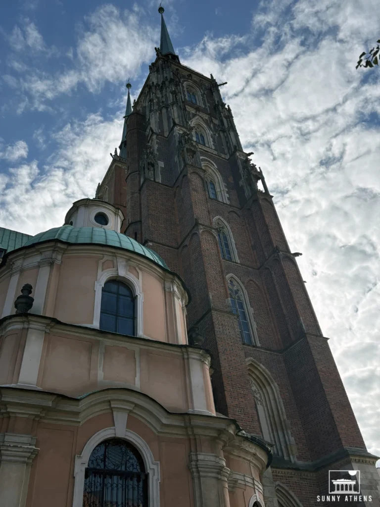 The towering Gothic facade of Wroclaw Cathedral under a partly cloudy sky.