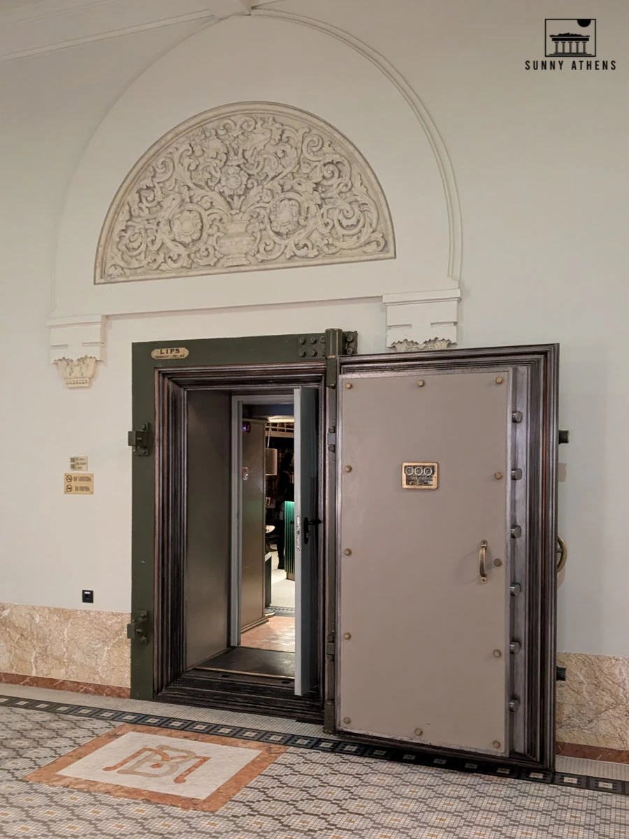 A large bank vault door stands open within an ornate marble-floored hall.