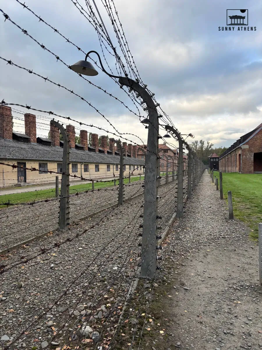 Barbed wire fence and gravel path leading past barracks at Auschwitz-Birkenau concentration camp.