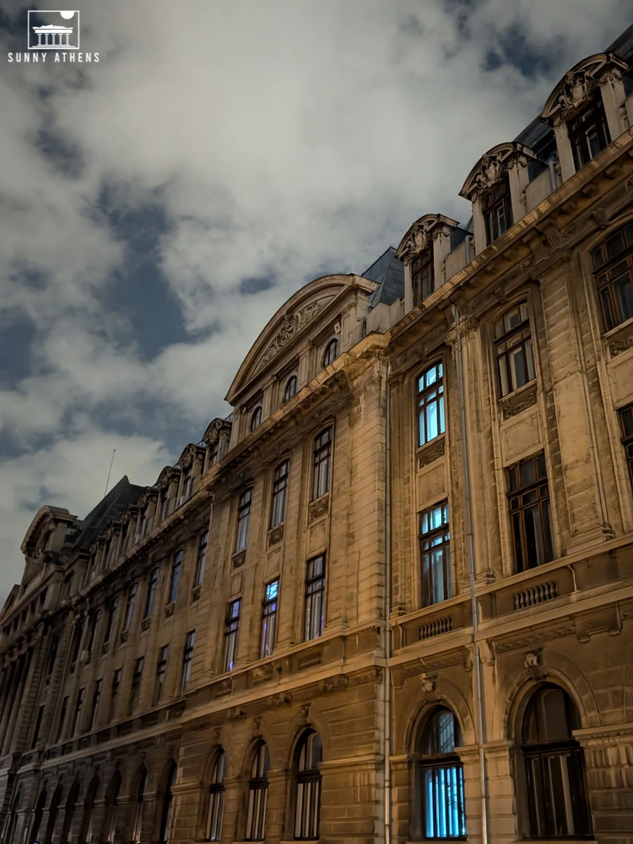 The National Museum of Romanian History building at night, illuminated with a warm glow against the cloudy sky.