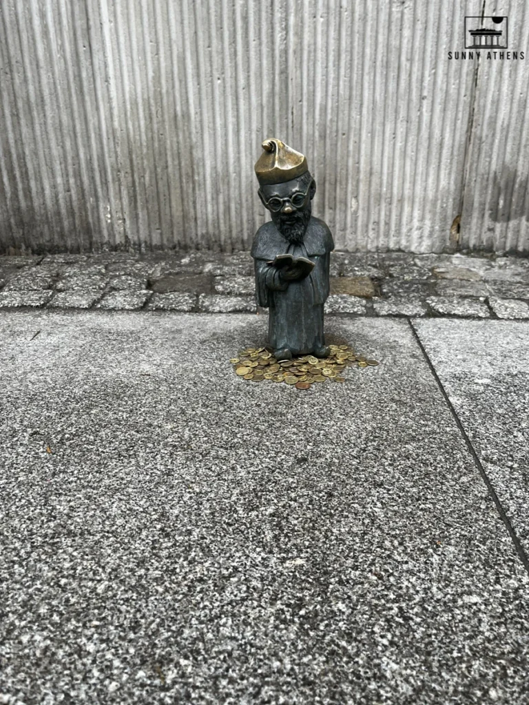 One day in Wroclaw Itinerary: small bronze dwarf statue holding a book on a stone pavement.