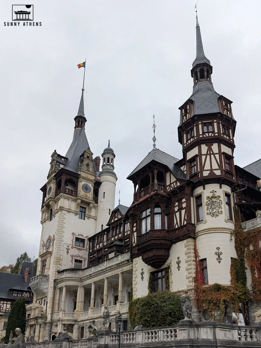 The magnificent Peles Castle with tall towers and a Romanian flag on top.
