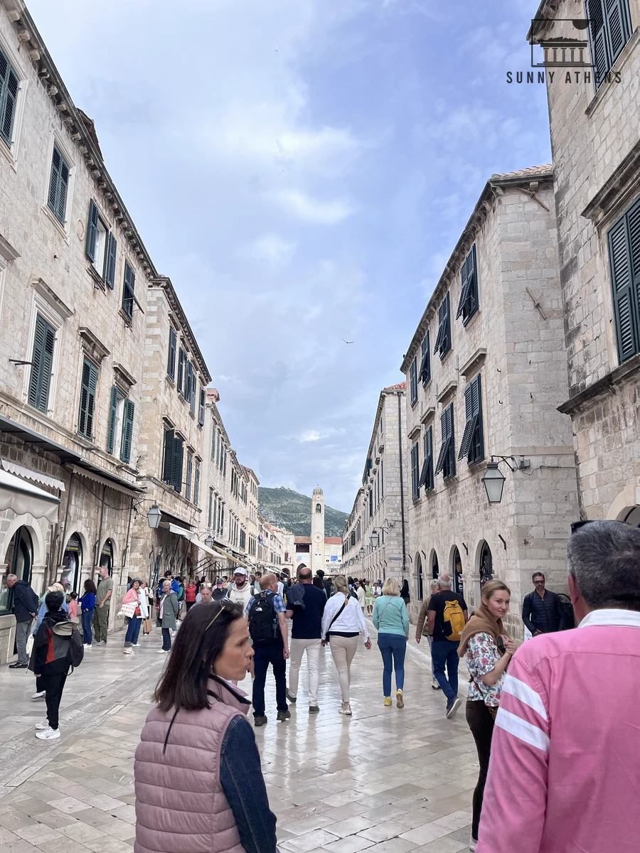 Travelers strolling along the polished limestone paving of Stradun pedestrian street lined with historic stone buildings