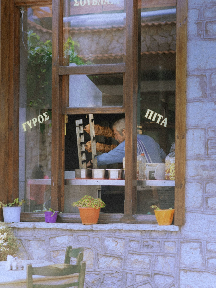 Traditional Greek souvlaki shop window with Greek lettering and a grillmaster inside